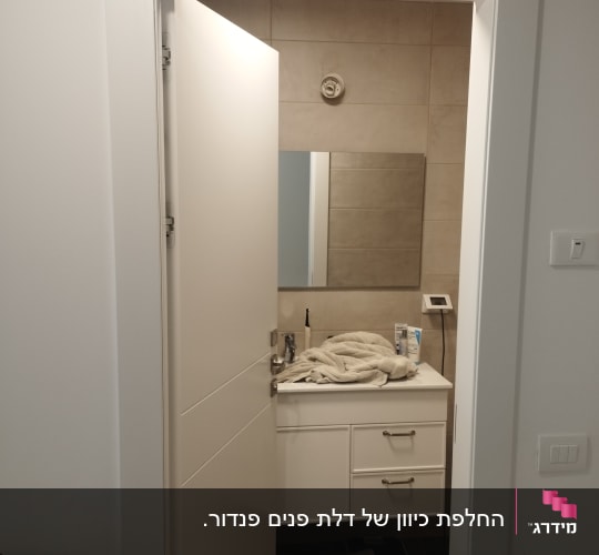 דלת פתוחה לחדר אמבטיה עם כיור ומראה